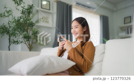 Happy young asian woman relax on comfortable couch at home texting messaging on smartphone 123770326