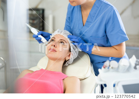 Young girl getting facial rf-lifting procedure of smoothes wrinkles and tightens skin on face in beauty salon. Concept of professional cosmetology Young girl getting facial rf-lifting procedure of smoothes wrinkles and tightens skin on face in beauty salon. Concept of professional cosmetology 123770542