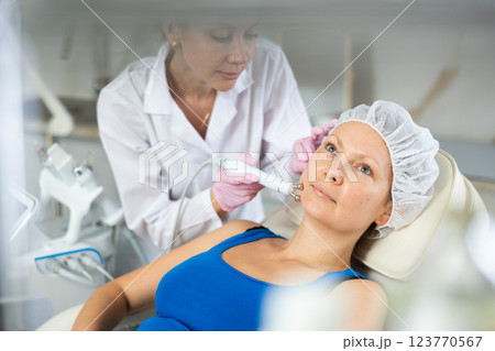 Young doctor doing RF lifting procedure for face lifting of adult woman laying in spa center. Smoothes wrinkles and tightens skin machine Young doctor doing RF lifting procedure for face lifting of adult woman laying in spa center. Smoothes wrinkles and tightens skin machine 123770567