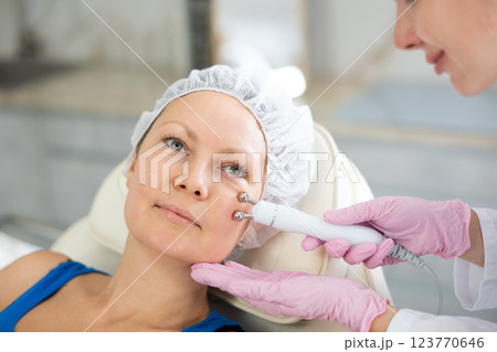 Young female cosmetologist doing microcurrent procedure to adult woman 123770646