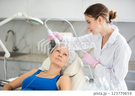 Young doctor use macromolecule atomizing pen for atomized nutrients to supplement and face skin nutrition for woman in cosmetology clinic. Moisturizing and rejuvenating hardware procedures Young doctor use macromolecule atomizing pen for atomized nutrients to supplement and face skin nutrition for woman in cosmetology clinic. Moisturizing and rejuvenating hardware procedures 123770659