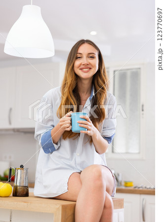 Portrait of happy young woman in shirt drinking morning coffee in modern kitchen 123770697