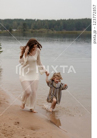 Mother and daughter walking barefoot in the water on the shore of a lake. 123772857