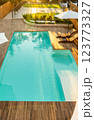 Luxurious turquoise swimming pool with wooden deck, umbrellas, and lounge chairs in a serene backyard setting 123773327