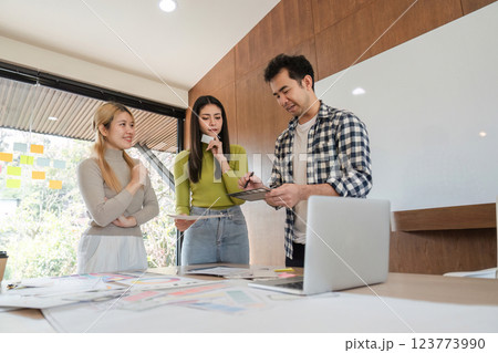 Diverse design team discussing project ideas using digital tablet in modern office. 123773990