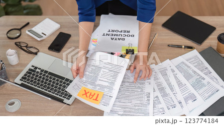 Accountant sorting tax paperwork and using a laptop in a contemporary office setting. 123774184