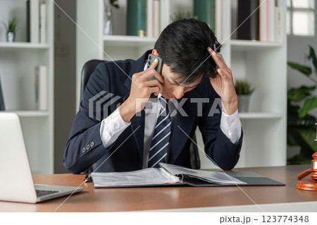 Frustrated lawyer on phone call while reviewing legal documents at desk in modern office. 123774348