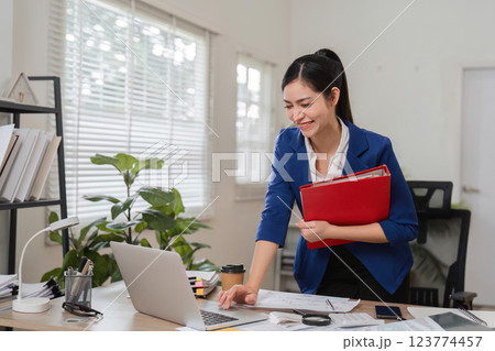 Businesswoman engaged in financial planning while holding a folder and using a laptop in her office. 123774457