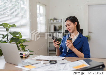 Businesswoman smiling while using smartphone and holding coffee in modern office 123774471