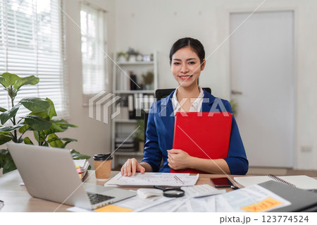 Businesswoman smiling while holding a red folder in her office 123774524