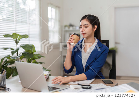 Businesswoman enjoying coffee while managing finances on her laptop. Businesswoman enjoying coffee while managing finances on her laptop. 123774527