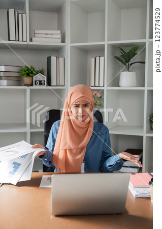 Diverse female accountant expressing confusion while reviewing financial reports on a laptop in an office. 123774529