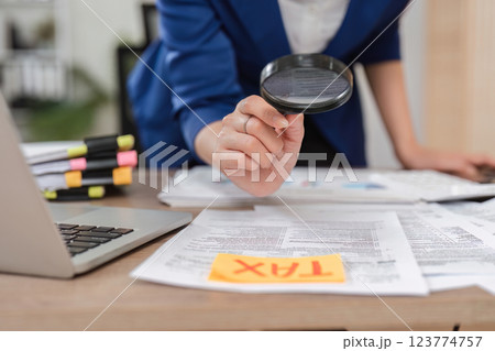 Close-up of an accountant using a magnifying glass on tax documents in a professional setting. 123774757