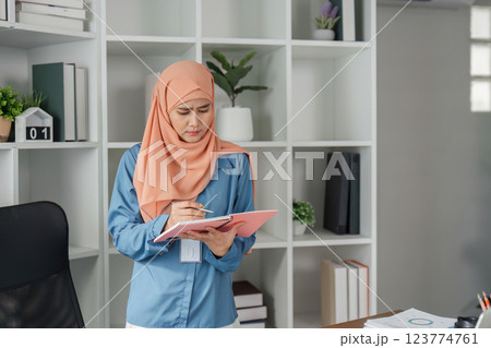 Muslim woman in hijab taking notes from documents in modern office. 123774761