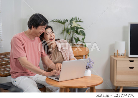 Joyful older couple sharing a laugh while using a laptop at home. 123774770