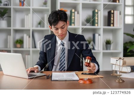 Young businessman using gavel to finalize decisions while reviewing documents in a modern office. Young businessman using gavel to finalize decisions while reviewing documents in a modern office. 123774926