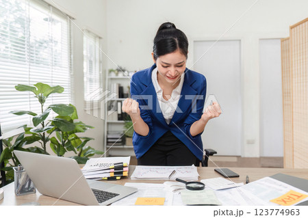 Businesswoman triumphantly celebrating her financial success and celebrating financial achievements at her desk 123774963