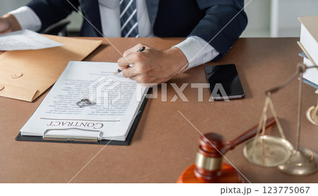 Lawyer signing contract document at desk, preparing legal agreement with gavel and scales of justice nearby. Lawyer signing contract document at desk, preparing legal agreement with gavel and scales of justice nearby. 123775067