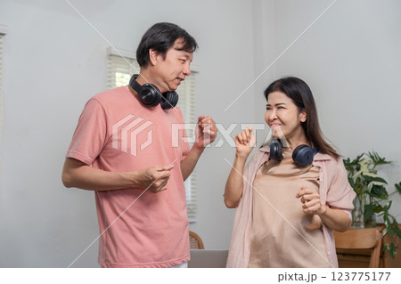Playful middle-aged couple enjoying music and dancing indoors with headphones. 123775177