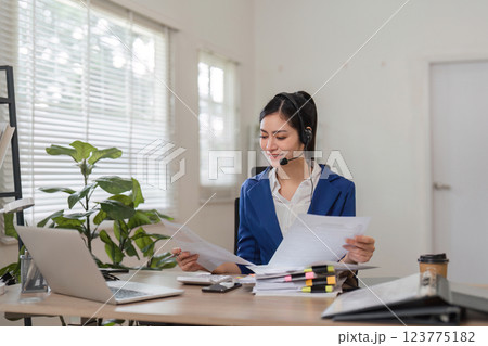Professional accountant managing tax documents and client calls in a modern office setting. Professional accountant managing tax documents and client calls in a modern office setting. 123775182