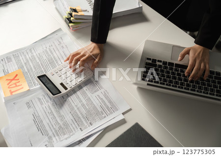 Businesswoman using a calculator for tax calculations while managing financial documents. 123775305