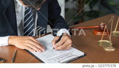 Lawyer reviewing and signing contract documents with gavel and scales of justice on desk. 123775376