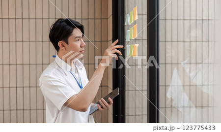 Young professional analyzing sticky notes on glass wall, organizing tasks and planning workflow in modern office. Young professional analyzing sticky notes on glass wall, organizing tasks and planning workflow in modern office. 123775433
