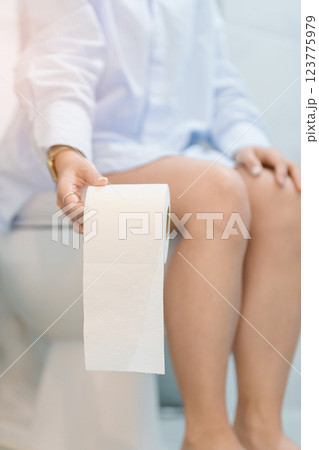 Woman holding toilet paper roll while sitting on toilet bowl. digestion, constipation, Diarrhea from food poisoning, infection, abdominal, stomachache, cystitis, Insurance, Health care and Medical 123775979