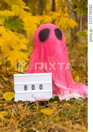 Trick or treat halloween pink ghost made of bandages with Lightbox BOO text in fall autumnal forest. Halloween greeting card. Handicraft handmade diy Trick or treat halloween pink ghost made of bandages with Lightbox BOO text in fall autumnal forest. Halloween greeting card. Handicraft handmade diy 123776082