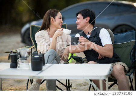 A woman and man is smiling at each other while holding their cup at folding table on camping ground A woman and man is smiling at each other while holding their cup at folding table on camping ground 123778196