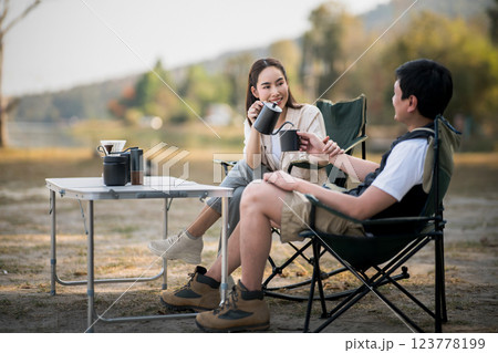 A woman is smiling at the man while pouring drink at folding table, with blurred forest scenery. A woman is smiling at the man while pouring drink at folding table, with blurred forest scenery. 123778199