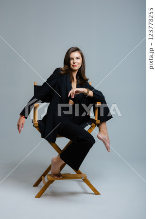 Young businesswoman posing on director chair wearing black suit and lace bra Young businesswoman posing on director chair wearing black suit and lace bra 123778255