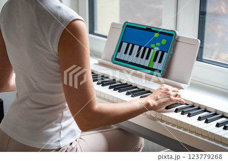 Young woman learning to play the keyboard at home using an interactive app. Using mobile apps for self-study concept 123779268