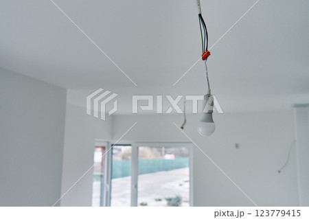 Single light bulb hanging from exposed electrical wires in unfinished interior with white walls and concrete flooring. Lighting in building under renovation Single light bulb hanging from exposed electrical wires in unfinished interior with white walls and concrete flooring. Lighting in building under renovation 123779415