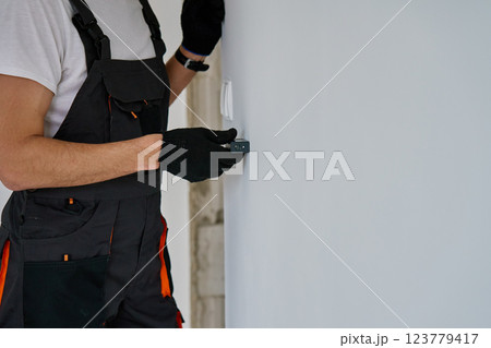 Construction worker in gloves uses laser distance measurer to inspect wall. Builder using digital tool for precision measurement during repair work. Construction and renovation concept Construction worker in gloves uses laser distance measurer to inspect wall. Builder using digital tool for precision measurement during repair work. Construction and renovation concept 123779417
