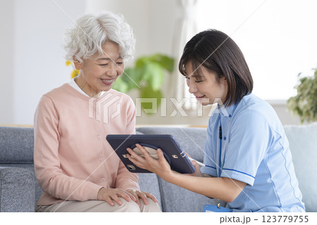 タブレットを持ってシニア女性の話を聞く介護スタッフ 123779755