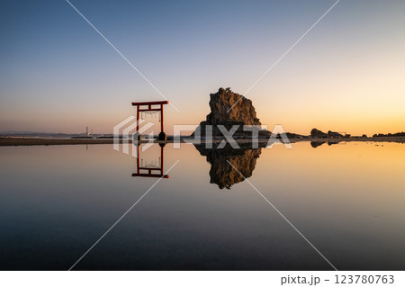 日の出を迎える海岸の鳥居と印象的な岩 123780763