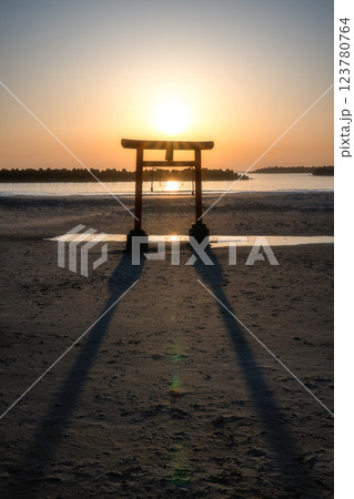 日の出を迎える海岸の鳥居と印象的な岩 123780764