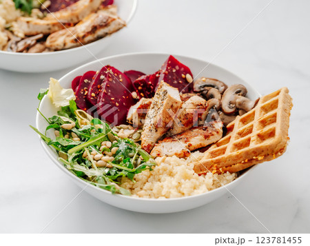 Bowl with grilled chicken, mushrooms, beetroot, quinoa, green rucola, decorated pine nuts and carrot waffle. Top view of gourmet bowl. Balanced gourmet dish on black wooden background. Healthy Food Bowl with grilled chicken, mushrooms, beetroot, quinoa, green rucola, decorated pine nuts and carrot waffle. Top view of gourmet bowl. Balanced gourmet dish on black wooden background. Healthy Food 123781455