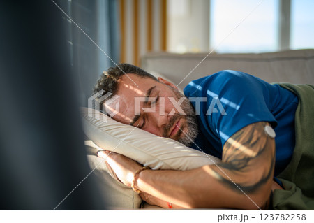 Diabetic man with CGM sensor on arm sleeping on sofa. 123782258
