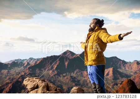 Young explorer reaching the mountain peak and meditating at the top, doing a zen meditation with calm and mindfulness. Happy content adventure seeker loving nature for self care. 123783128