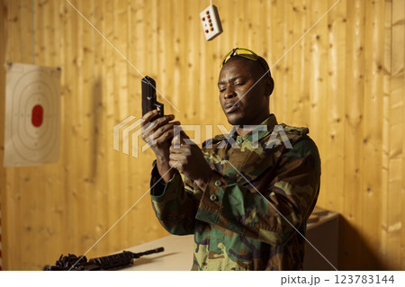 Army soldier in shooting range reloading pistol, preparing to shoot targets, readying for combat. Military unit at indoor shooting ground facility loading handgun, wearing protection gear Army soldier in shooting range reloading pistol, preparing to shoot targets, readying for combat. Military unit at indoor shooting ground facility loading handgun, wearing protection gear 123783144