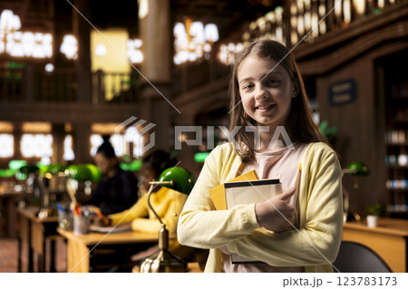Portrait of clever caucasian scholar posing with her textbooks in the library, feeling ambitious to finish school with perfect grades. Teenage girl preparing for her exams, academic focus. 123783173