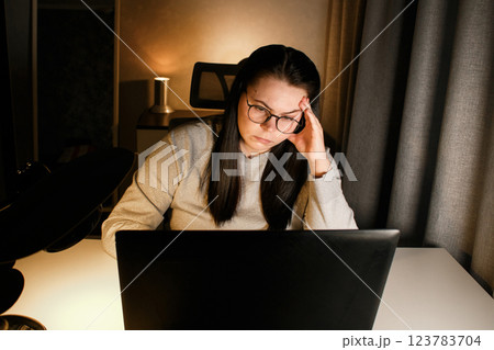 Young woman with eyeglasses working on laptop at home late at night, using modern technologies and getting online education. Remote learning concept. Online university. Focus on process. 123783704