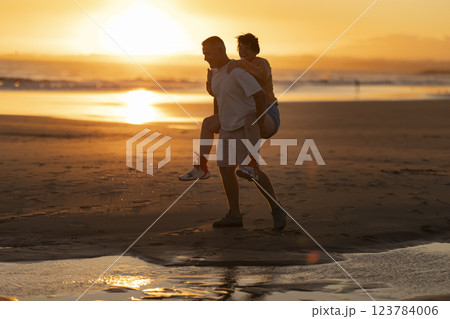 Happy senior couple piggybacking on beach at sunset 123784006