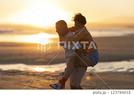 Happy couple piggybacking on beach at sunset Happy couple piggybacking on beach at sunset 123784018