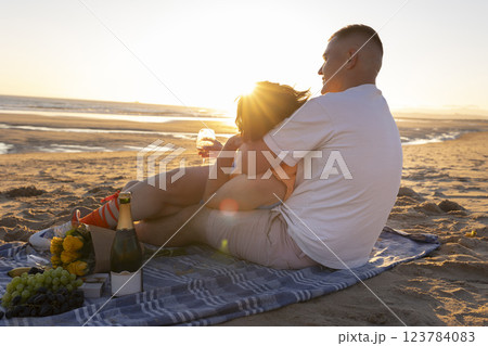 Couple enjoying romantic sunset picnic on beach with wine and flowers Couple enjoying romantic sunset picnic on beach with wine and flowers 123784083
