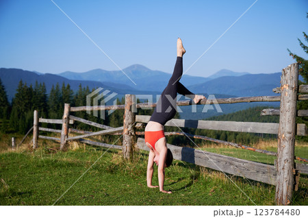 Woman practicing yoga outdoors in the mountains in a serene, natural setting. Female performing yoga pose, with backdrop of beautiful mountain landscape at sunrise or sunset. 123784480