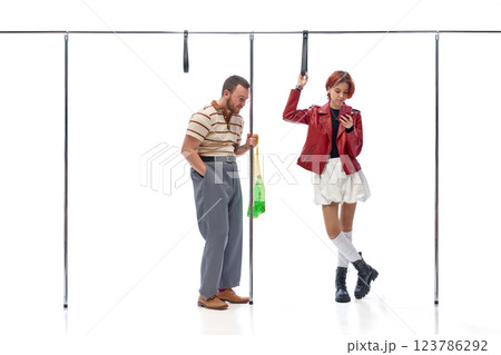 Young man holding shopping bag and woman in stylish outfit looking at phone while commuting against white background. Young man holding shopping bag and woman in stylish outfit looking at phone while commuting against white background. 123786292