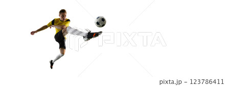 Dynamic image of man, soccer player in black shorts and yellow jersey in motion, kicking ball isolated on white background Dynamic image of man, soccer player in black shorts and yellow jersey in motion, kicking ball isolated on white background 123786411